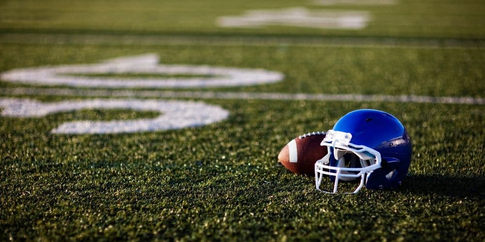 Blue football helmet and football on a green field with yard markers.